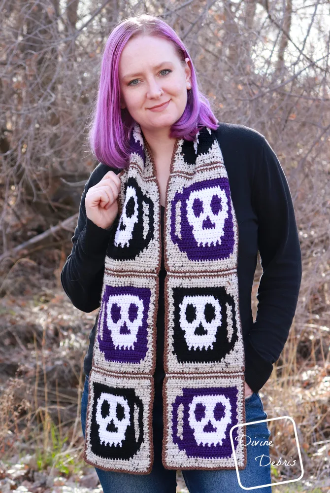 [Image description] A white woman with purple hair stands in front of trees with the Wake the Dead Scarf draped around her neck and down the front.