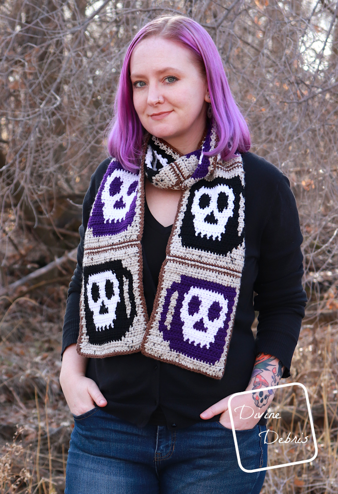 [Image description] A white woman with purple hair stands in front of trees with the Wake the Dead Scarf wrapped around her neck and down the front.