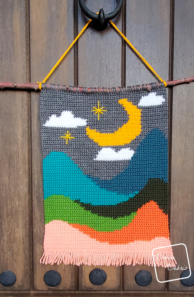 [Image description] Celestial Peaks Wall Hanging hanging against a wooden brown background.