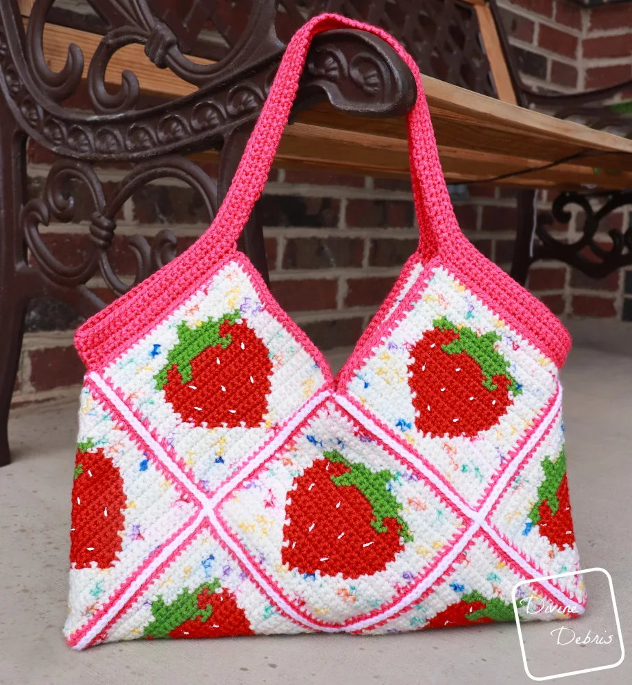 [Photo description] Close up of the Cute Strawberry Bag hanging from a bench, against a brick background..