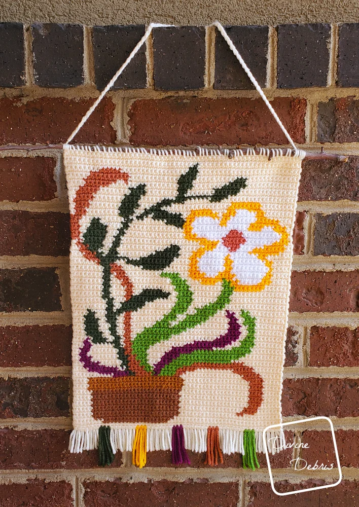 [Image description] Groovy Bloom Wall Hanging hanging against brick stone background.