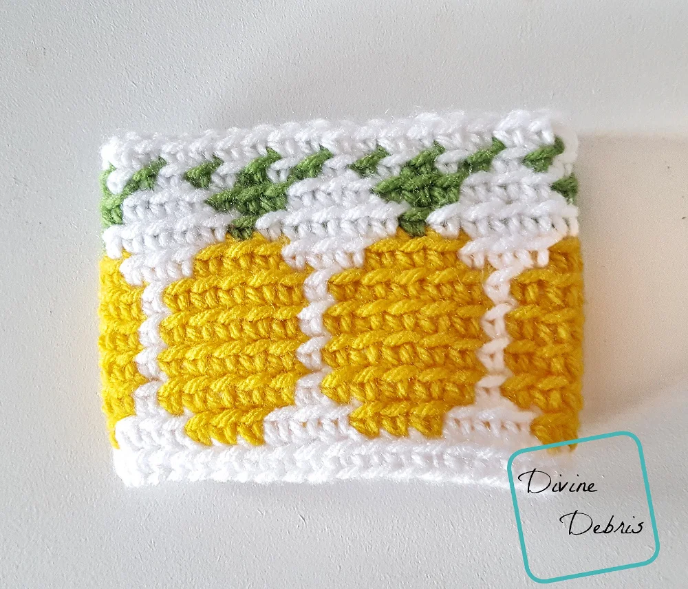 [Image description] the Pineapples Mug Cozy free crochet pattern lays flat on an off white surface.
