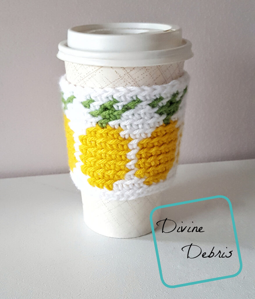 [Image description] the Pineapples Mug Cozy free crochet pattern sits on a to-go coffee cup against an off white background on an off white surface.