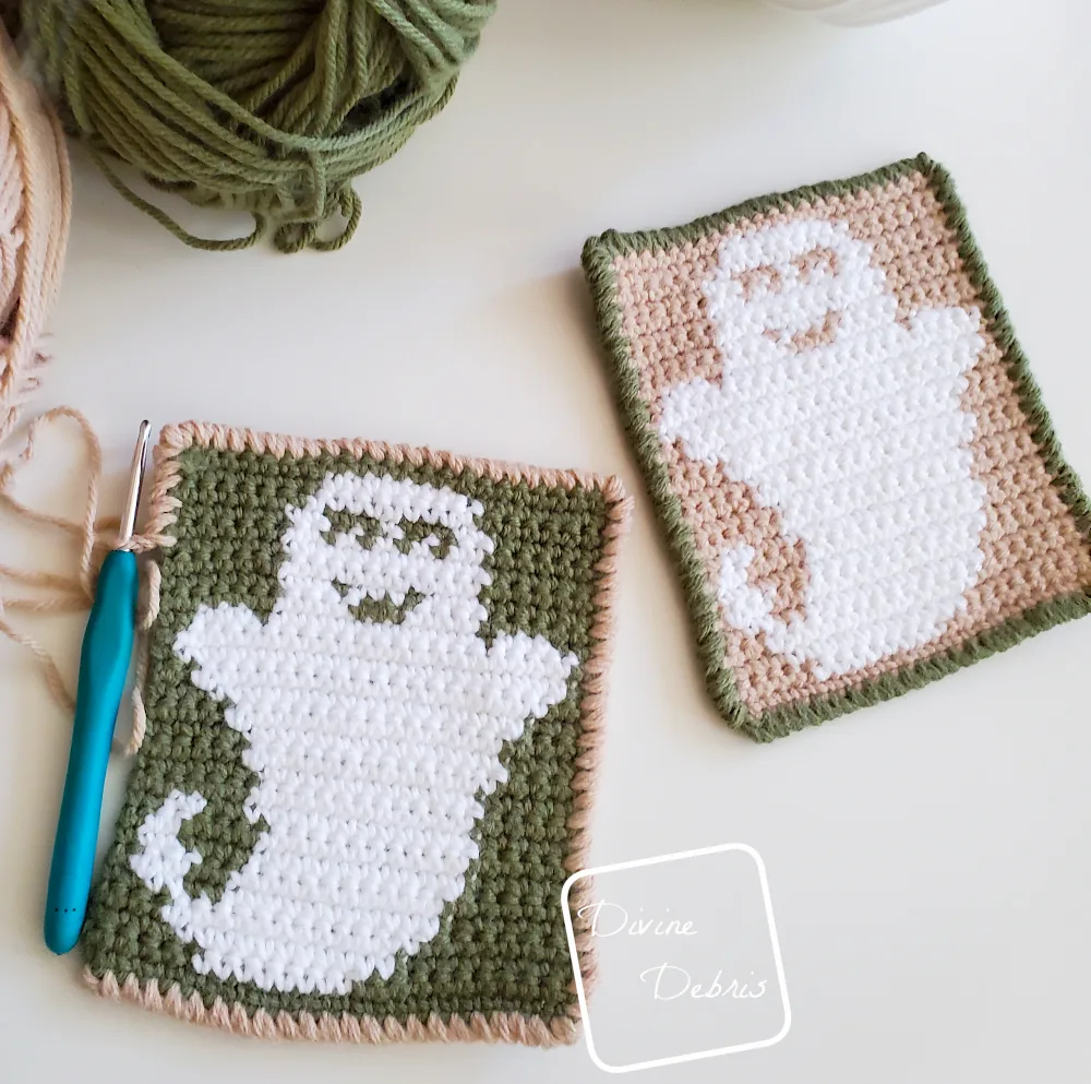 [Image description] A top down view of 2 Cute Ghost Coasters sitting on a white background, the green and ghost coaster on the left is unfinished with a crochet hook still working on the border.