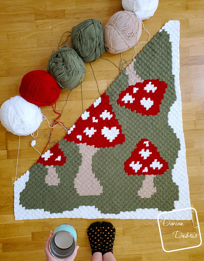 [Image description] Top down look at the unfinished Mushroom Love Blanket with skeins of yarn along the top left side of the photo.