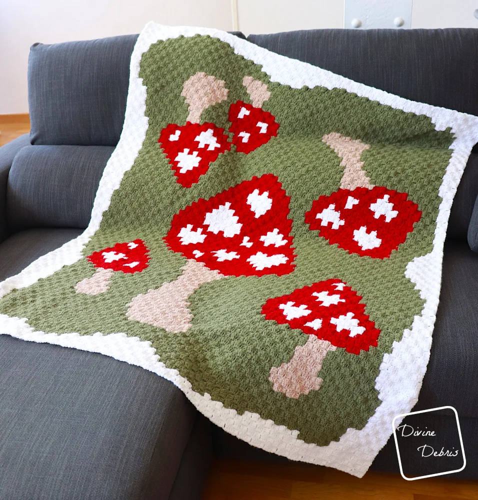 [Image description] The Mushroom Love Blanket lays at a slight angle on a gray couch, with white walls behind and tan floors below the couch.