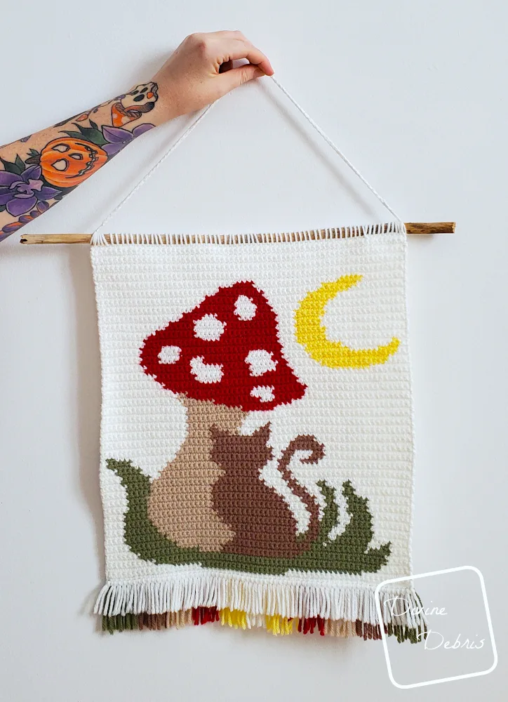 [Image description] Meow-Shroom Moon Wall Hanging being held by a white woman's arm against a white wall.