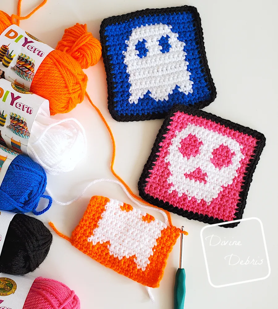 [Image description] Top down view of the Skull and Ghost Halloween Squares with skeins of yarn along the left side of the photo and an unfinished square at the bottom of the photo.