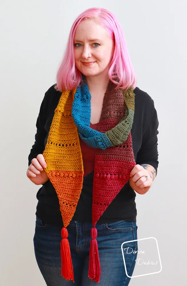 [Image description] A white woman with pink hair stands against a white wall wearing the Loretta Scarf looped around her neck and hanging long.