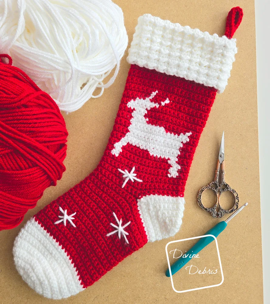 [Image description] The Twinkle Toes Reindeer Stocking on a tan background with a skein of red and a skein of white yarn along the top left of the frame.