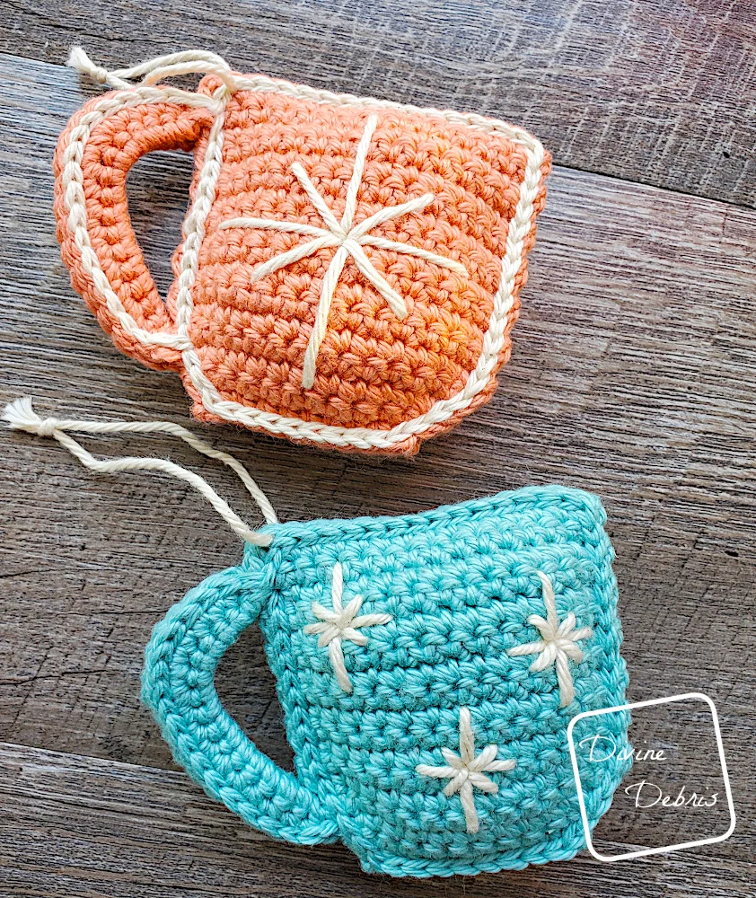 [image description] A close up of 2 Cute Cup Ornaments on a fake wood background.