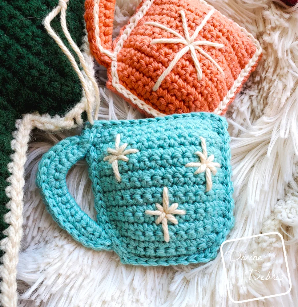 [Image description] A close up of a blue Cute Cup Ornament on a furry white background with an orange Cute Cup Ornament in the background.