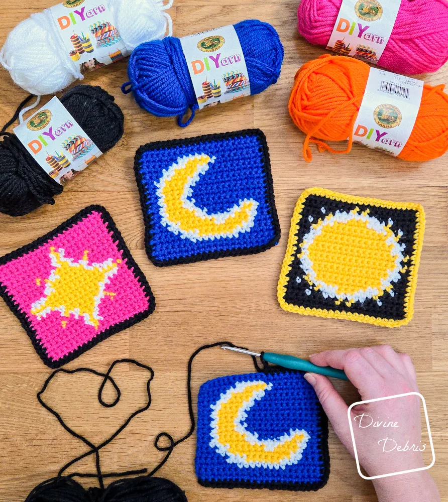 [Image description] top down view of 3 of the Galactic Glow Trio squares with skeins of yarn along the top of the photo and a white woman's hand holding a crochet hook working on a 4th square.