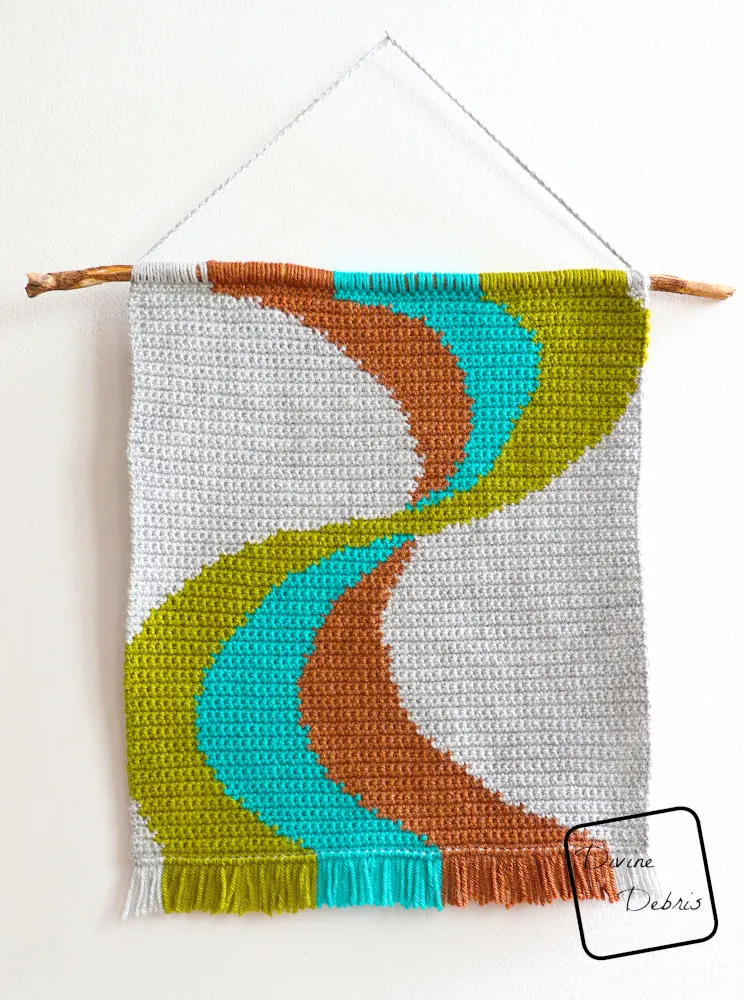 [Image description] The Color Swirl Wall Hanging, hanging on a white wall with light coming from the right side of the photo.