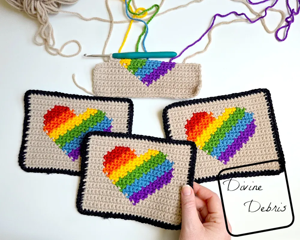 [Image description] 3 finished Rainbow Heart Coasters and one half finished coaster on a white background, with a white woman's hand holding the bottom coaster by the right-hand corner.