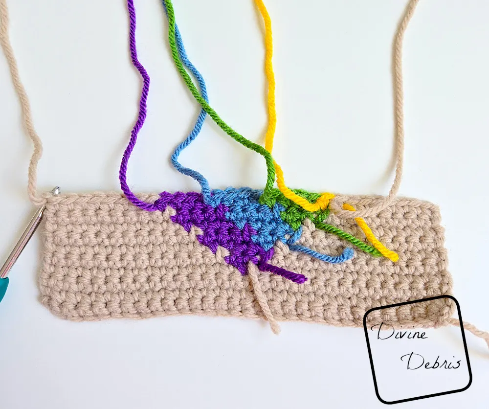 [Image description) a half done Rainbow Heart Coaster on a white background showing the individuals strands of color from the WS.