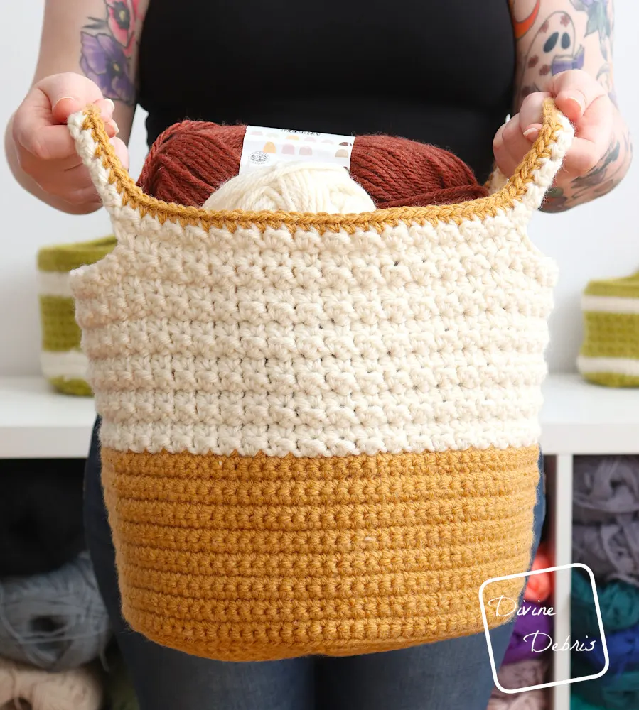 [Image description] A white woman's arms holding the Trudy Two-Tone Basket towards the camera in front of a white background
