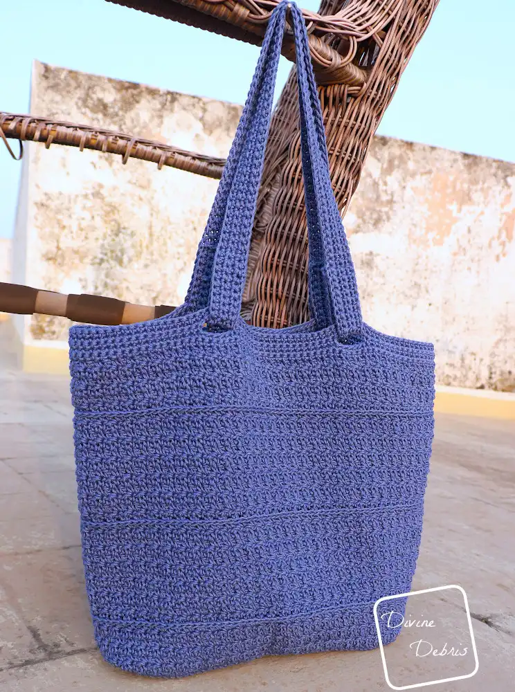 [Image description] A close up view of the Kieran Bag hanging from a wooden chair frame, from a upward angle position, against a speckled background.