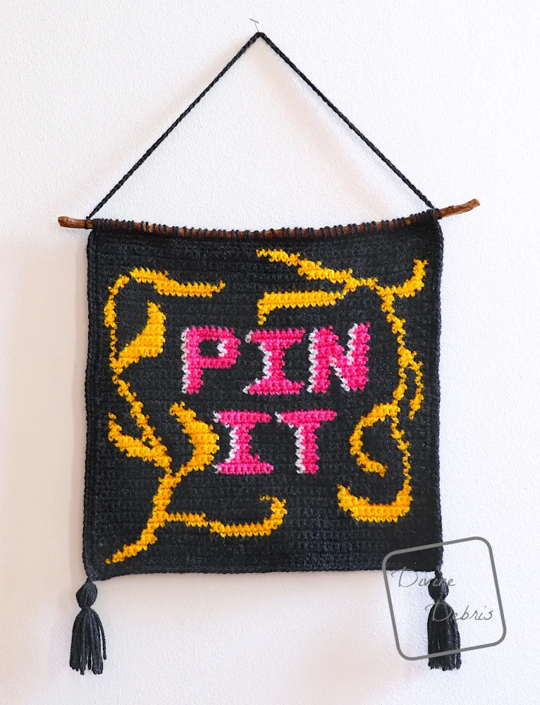 [Image description] The Pin It Wall Hanging hangs on a pin up against a white wall.