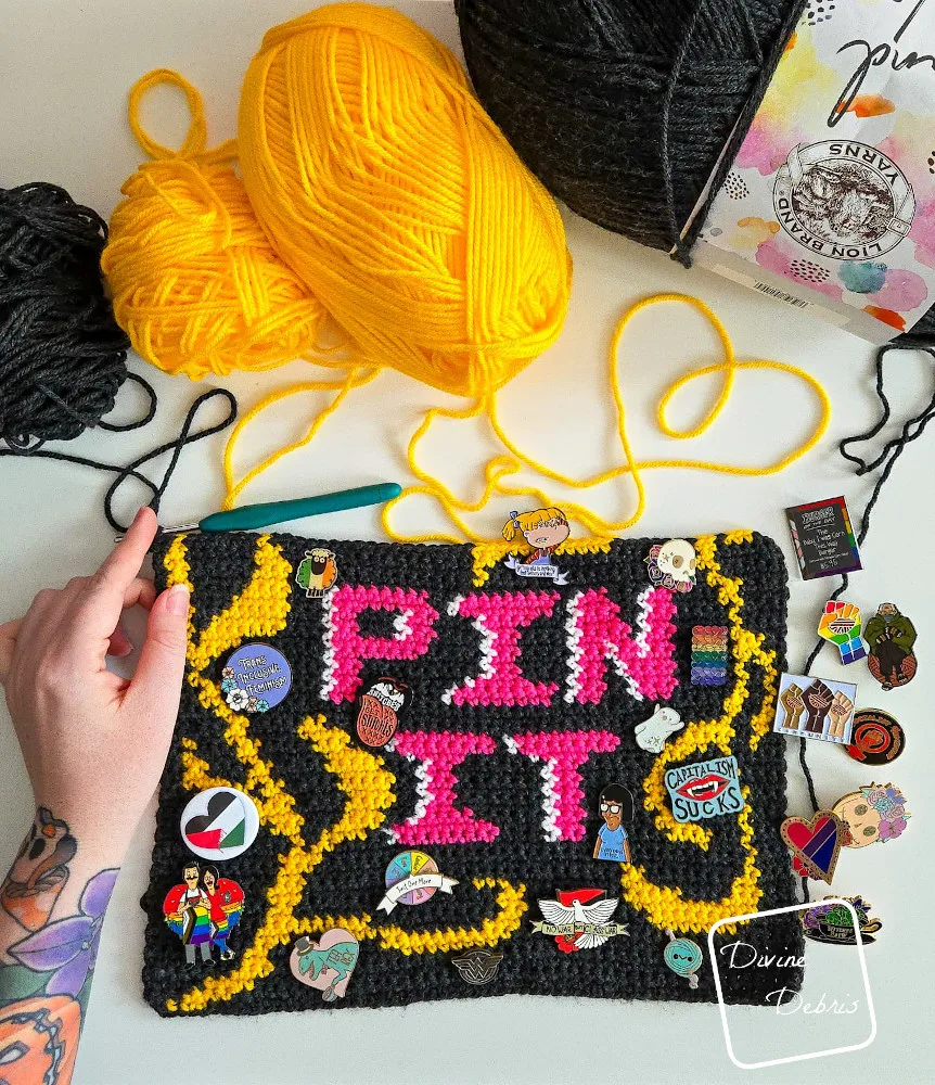 [Image description] An unfinished version of the Pin It Wall Hanging with pins on it and a white woman's hand holding the left side. 