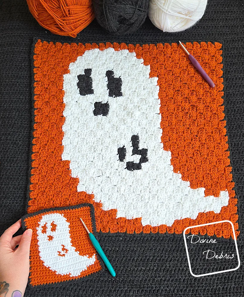 [Image description] Top down view of both versions of the Gwendoline Ghost Squares crochet patterns, on a black background and a white woman's hand holding the smaller square in the bottom left corner. 