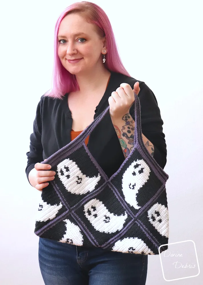 [Image description] A white woman with pink hair stands in front of a white wall holding the Gwendoline Ghost Bag up towards the camera.