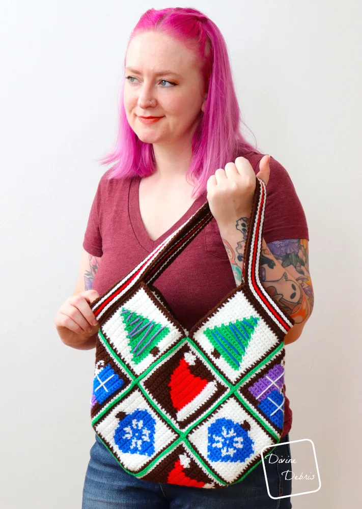 [image description] A white woman with pink hair stands looking to her right against a white wall holding the Patchwork Christmas Bag up to the camera.