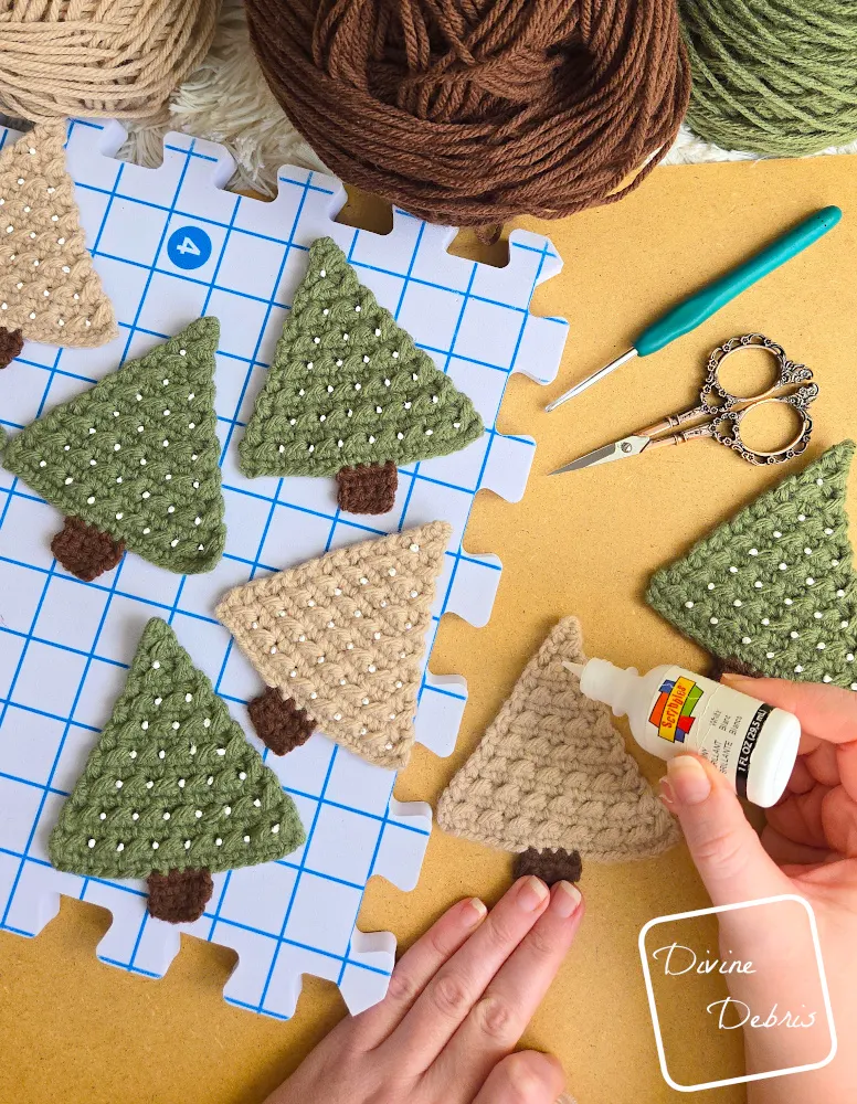 [Image description] Top down look of a white woman's hands adding puffy paint dots to trees for the Cute Tree Garland crochet pattern.