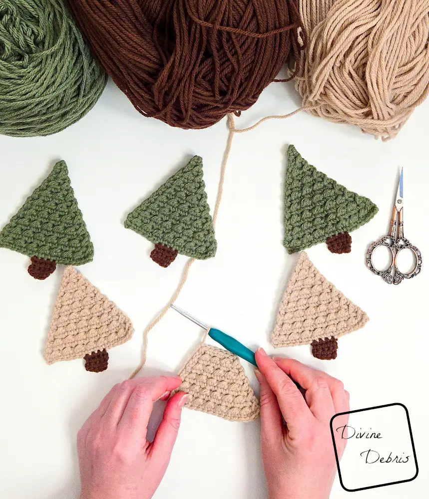 [Image description] Top down view of a white woman's hands working on a tan Cute Tree Applique, surrounded by other trees for the garland on a white background.