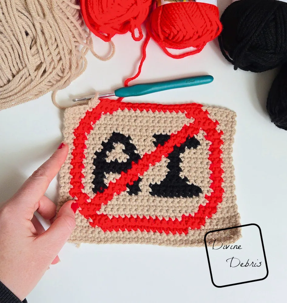 [Image description] An unfinished Anti AI Wall Hanging sits on a white background with skeins of yarn along the top of the photo and a white woman's hand holding the bottom left corner.