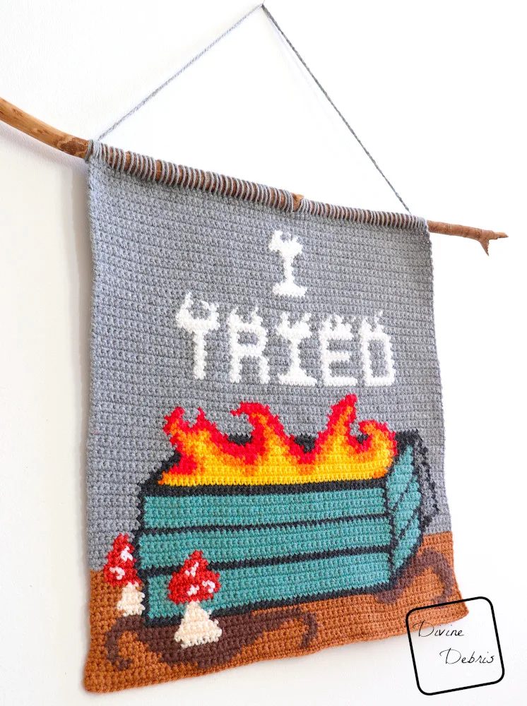 [Image description] The I Tried Dumpster Fire Wall Hanging hangs on a white wall, photo taking from an angle.