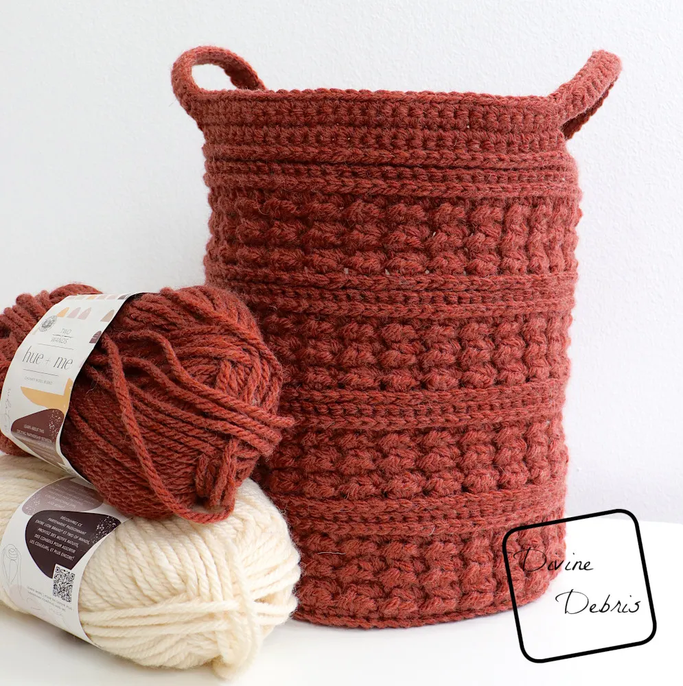 [Image description] The Lucy Basket crochet pattern sits in front of a white background on a white shelf with 2 skeins (white and red) of yarn on the left side of the basket